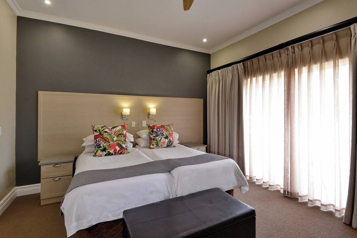 A hotel room with a large bed, two bedside tables, a bench, and a window with curtains.