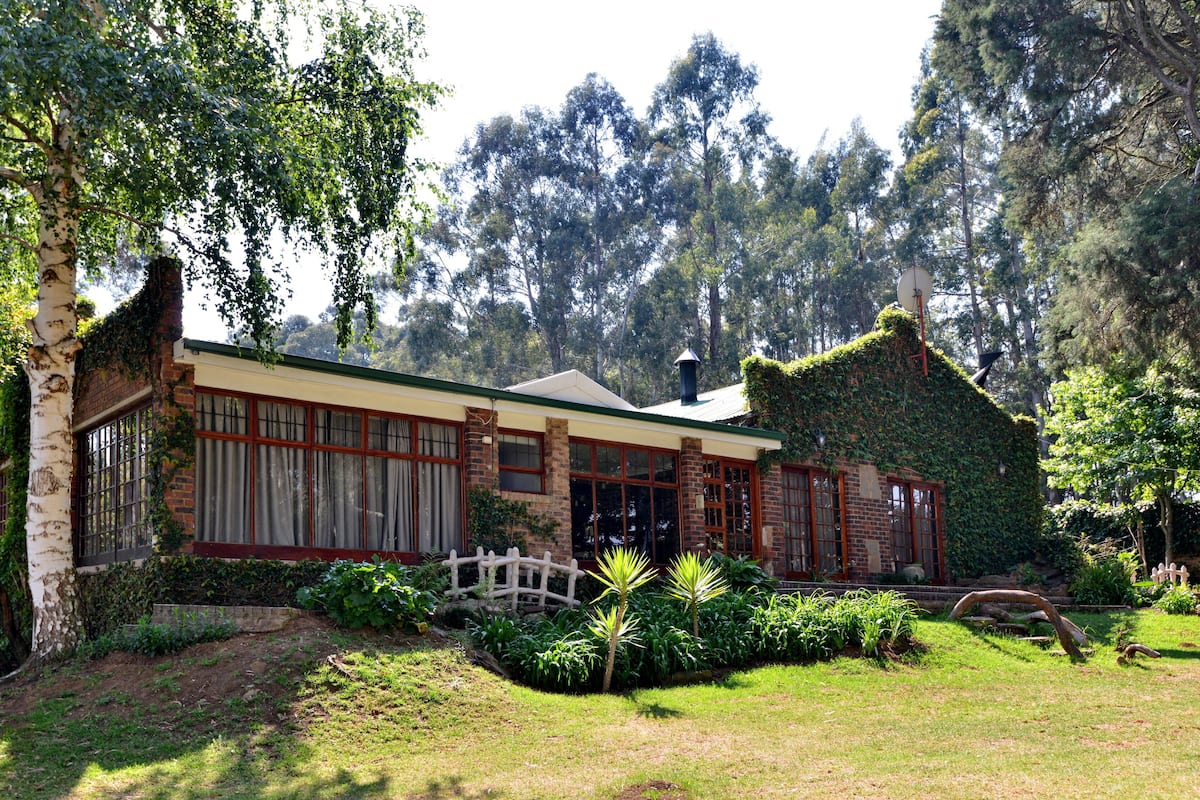 A house with a brick exterior, large windows, and a garden with various plants and a small fence.