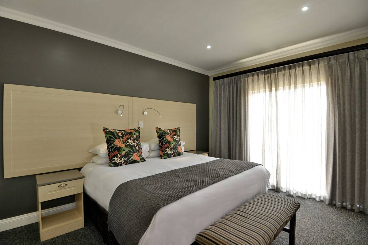 A hotel room with a large bed, bedside tables, a bench, and a window with curtains.