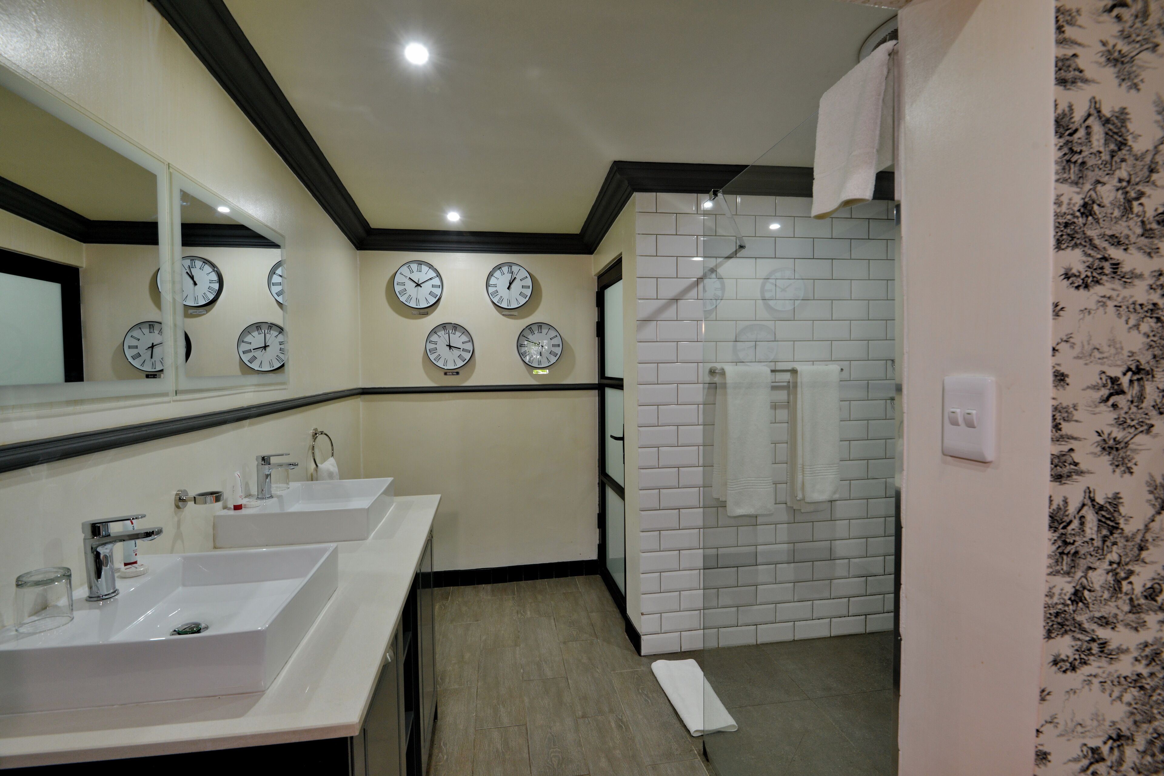A bathroom with two sinks, a mirror, and multiple wall clocks.