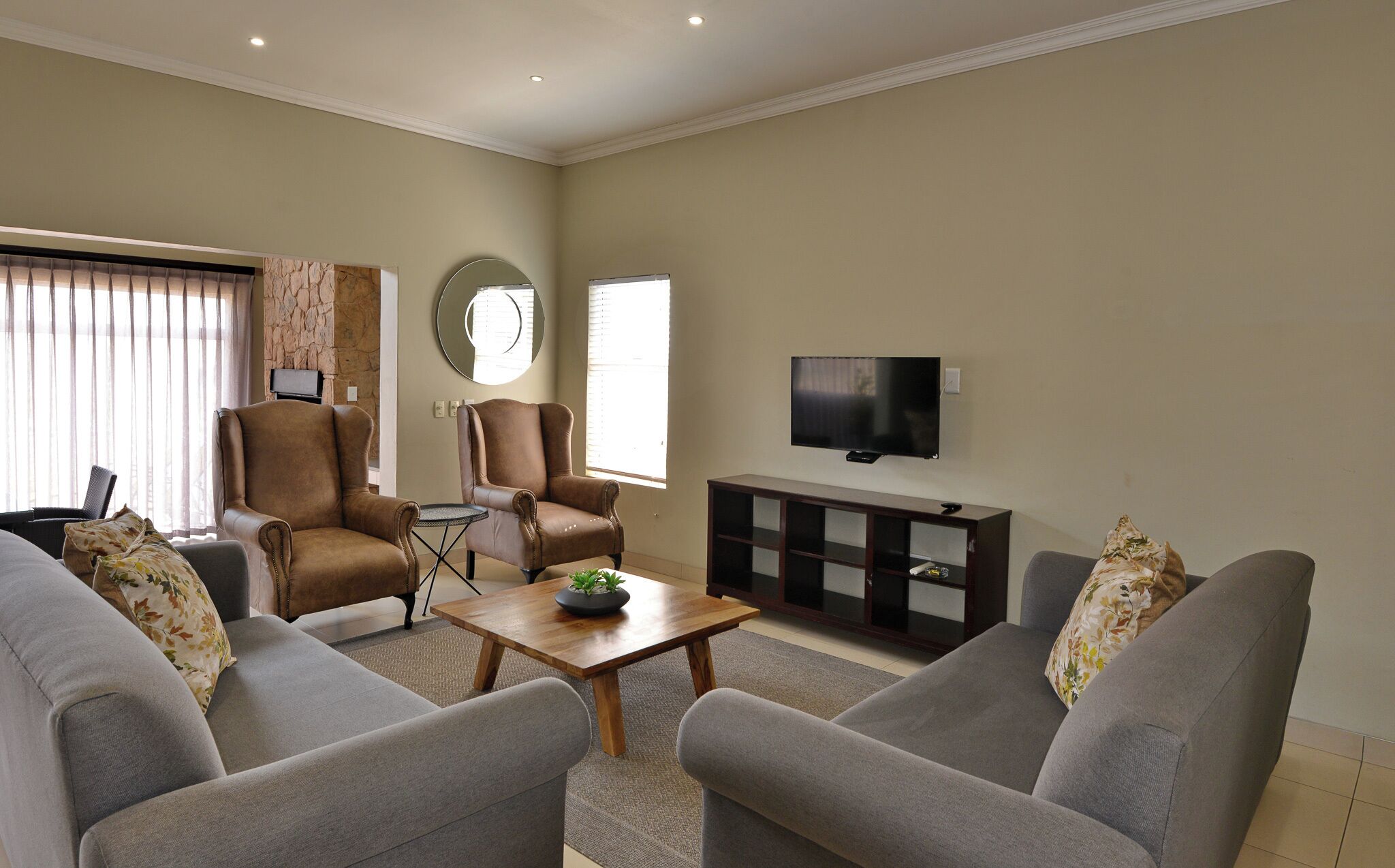 A living room with two grey sofas, a wooden coffee table, a TV on a stand, and a stone accent wall.