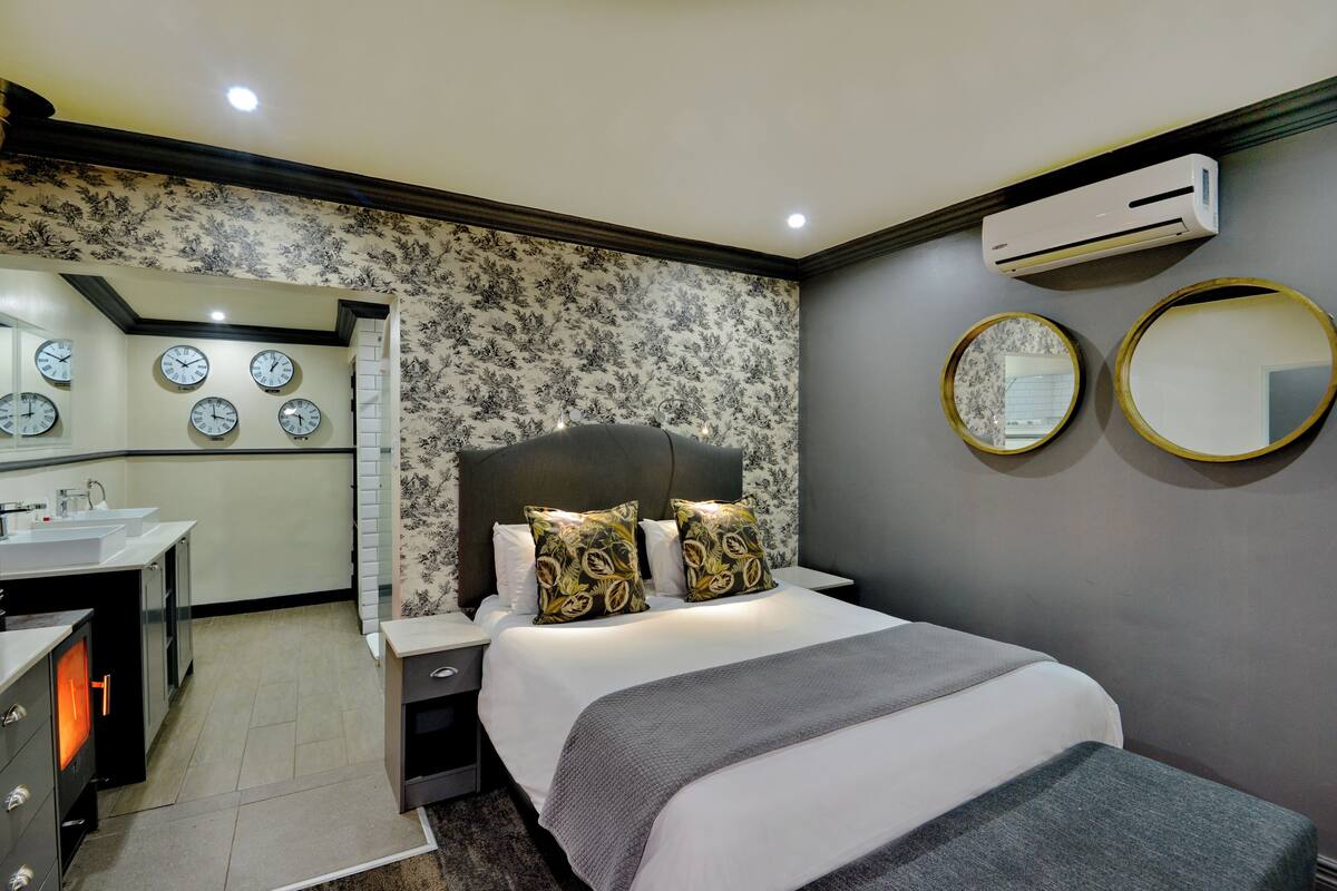 A modern hotel room with a bed, bedside tables, a mirror, and a wall-mounted air conditioner.