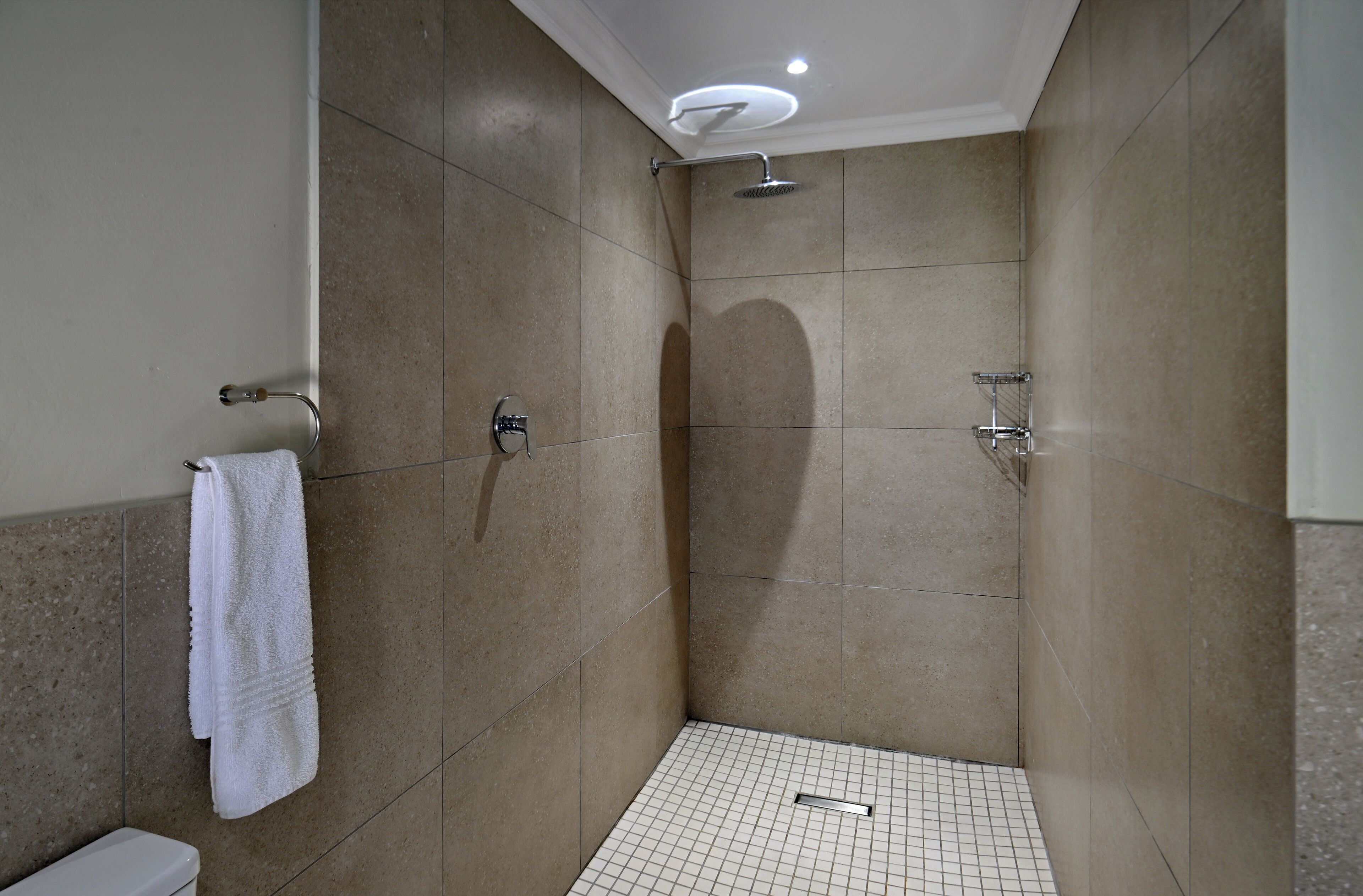 Une douche à l’italienne avec des carreaux de couleur beige, une serviette blanche suspendue à un porte-serviettes et un sol à motifs géométriques.