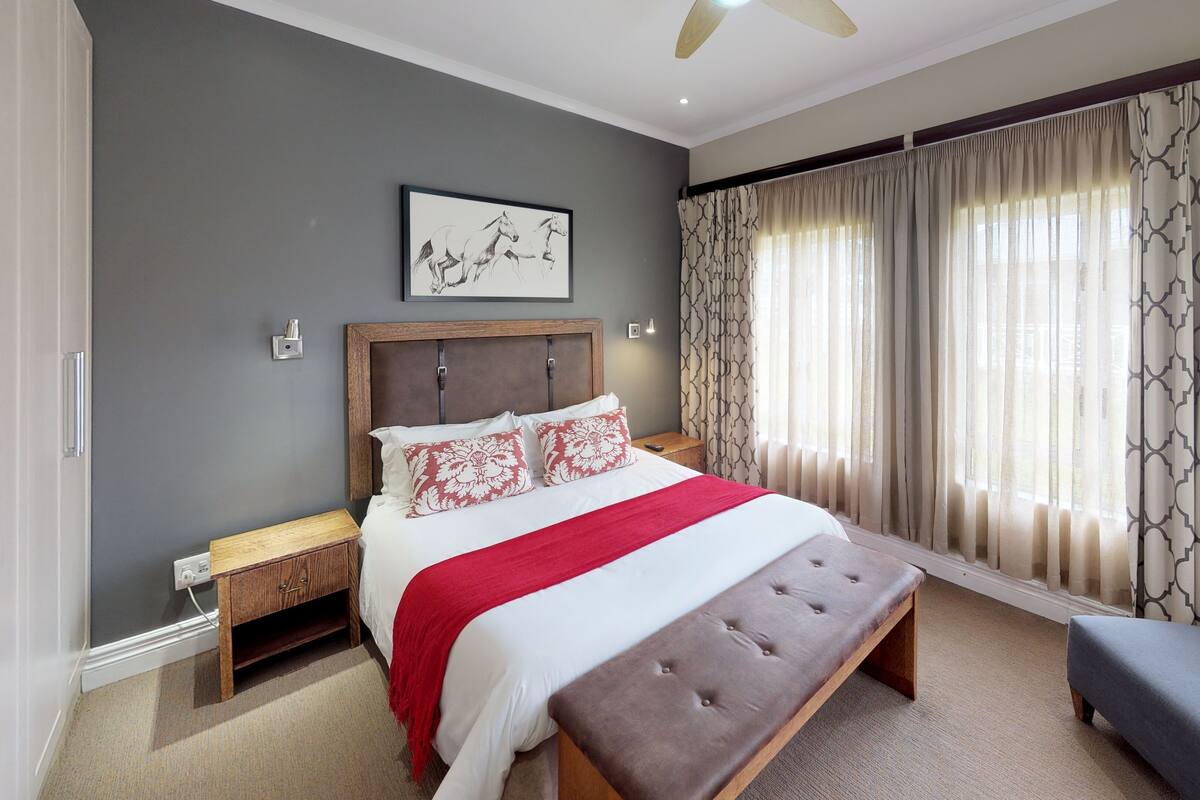 A bedroom with a large bed, a wooden headboard, a bench, a chair, and a ceiling fan.