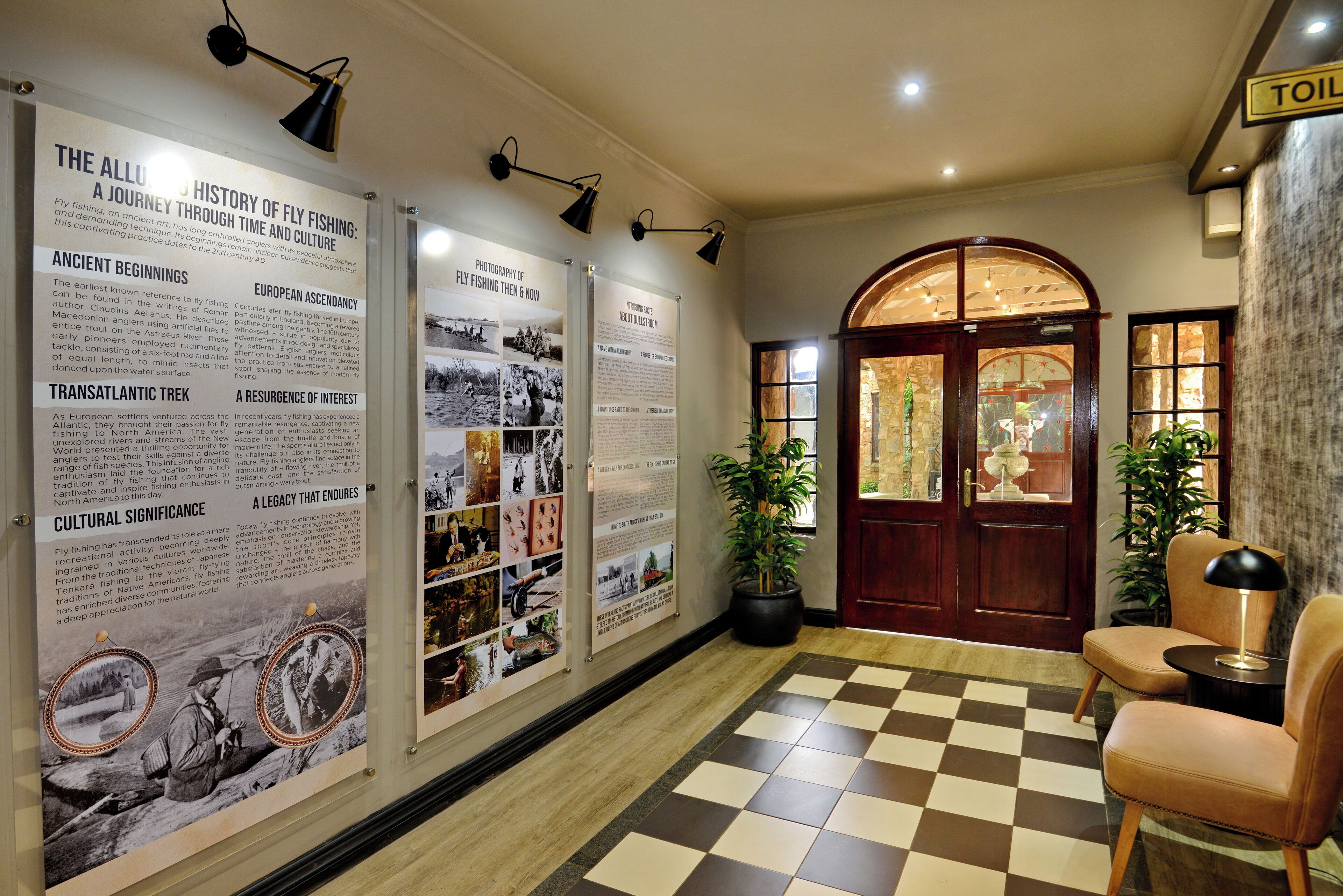A hallway with informational posters, a checkered floor, a wooden door, and a seating area with a lamp.