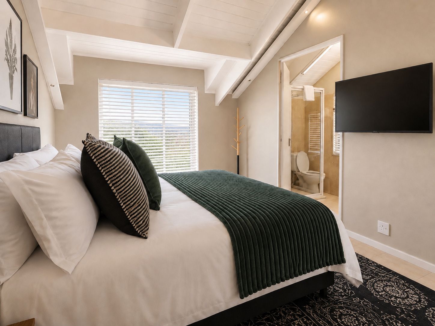 Un dormitorio con cama, televisión y baño visible a través de una puerta abierta.