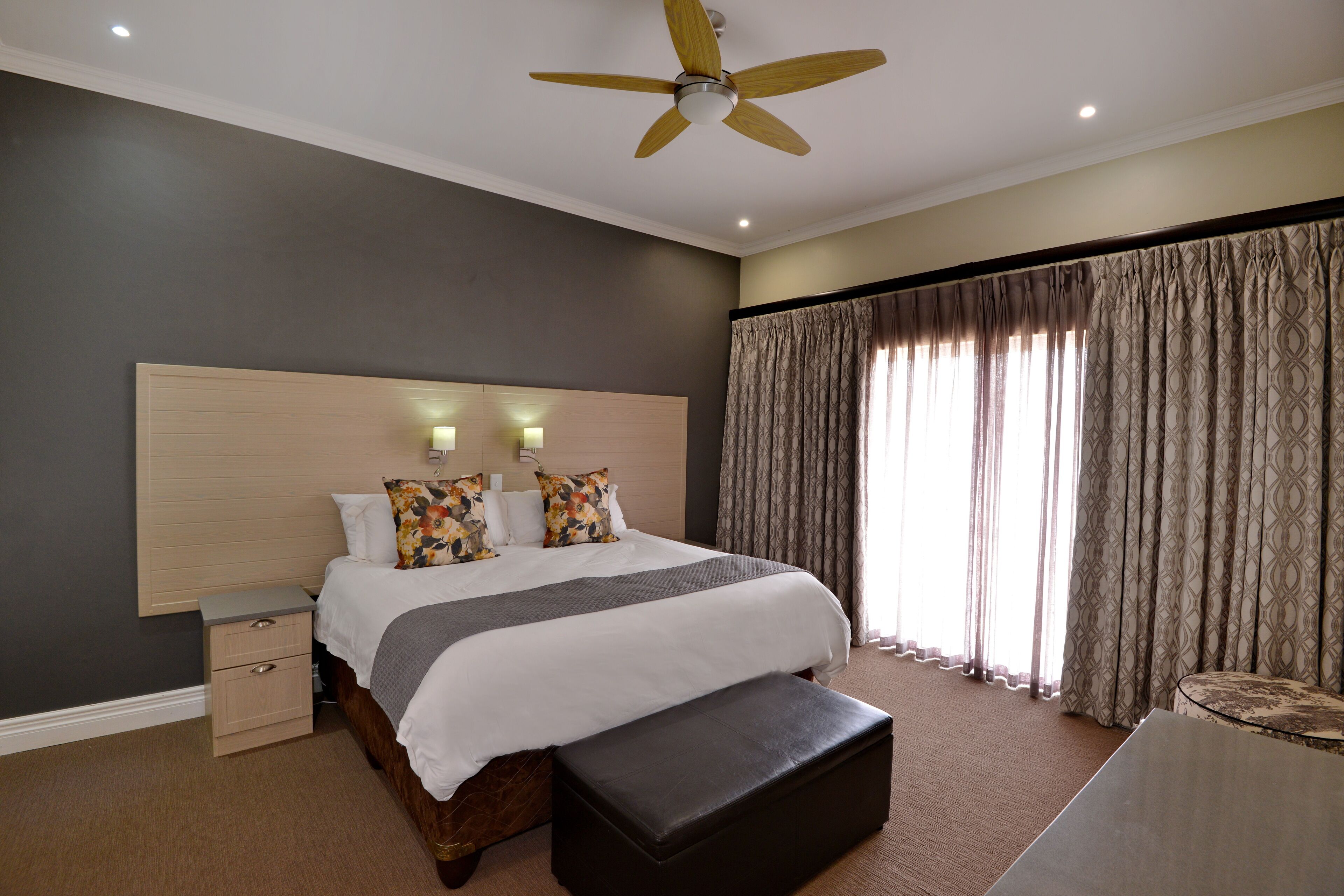 A bedroom with a bed, bedside tables, a ceiling fan, and a large window with curtains.