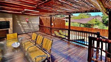 An outdoor patio with a glass table, wicker chairs, a barbecue grill, and a view of a swimming pool.