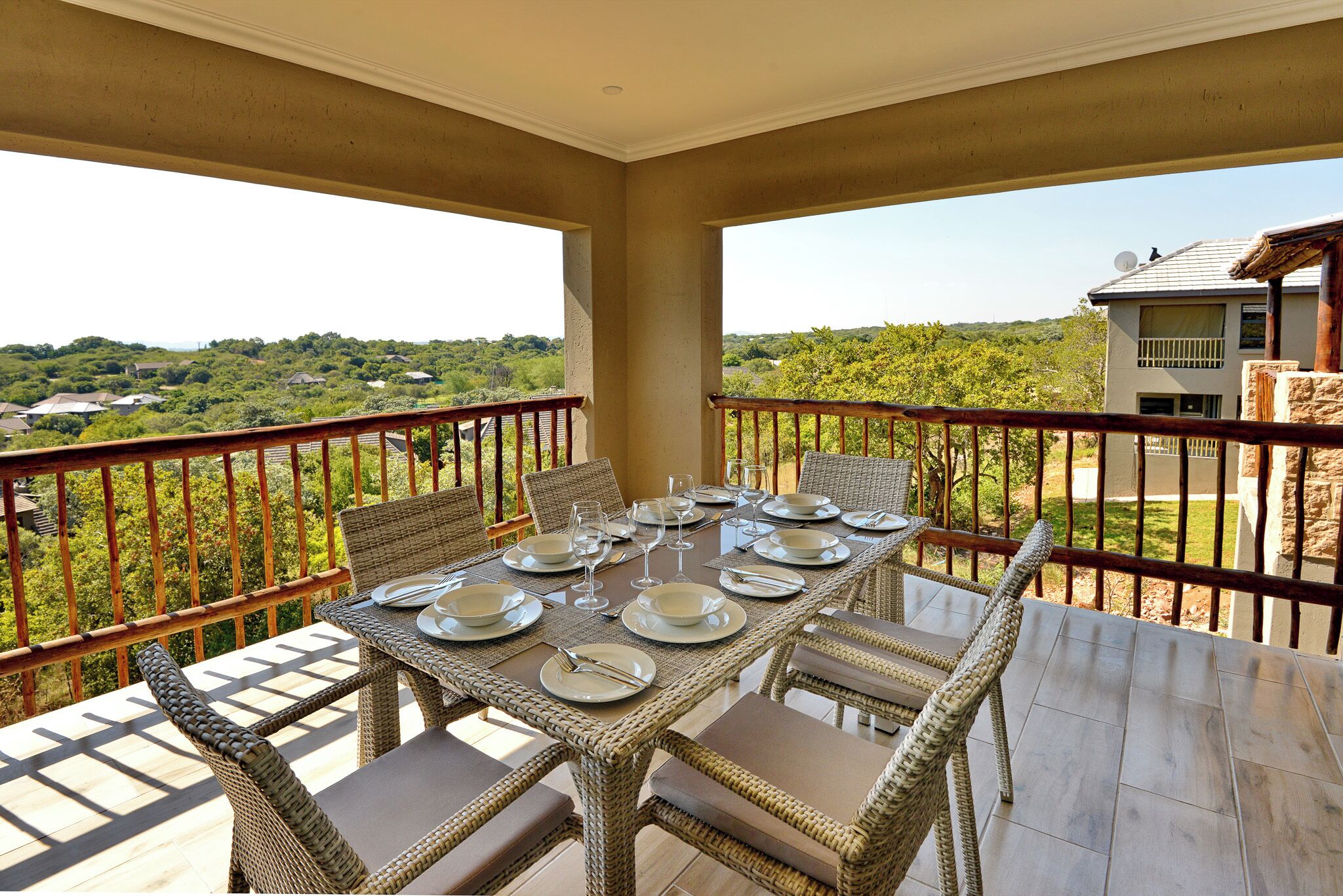 Un balcon avec une table à manger dressée pour six personnes, entouré de chaises en osier.