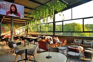 A restaurant with multiple seating areas, including round tables and sofas, and large windows offering a view of the outdoors.