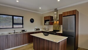 A modern kitchen with wooden cabinets, a stainless steel refrigerator, a microwave, and a sink. - Seasons Golf, Leisure & Spa (Hartbeespoort/ Brits)