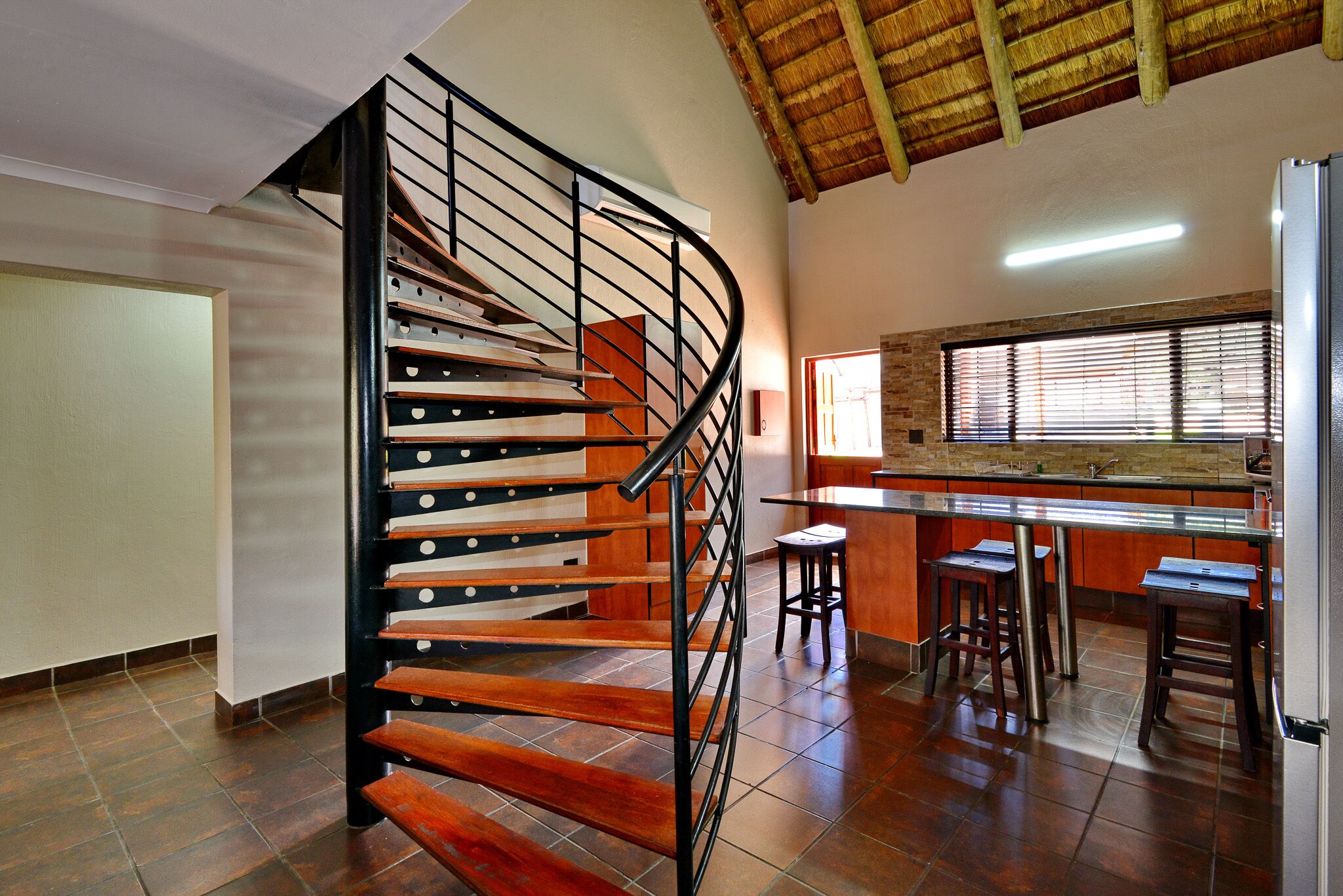 A modern kitchen with a central island, a built-in stove, and a large window with blinds.
