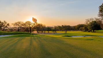 A golf course with a flagstick, trees, and a clear sky.