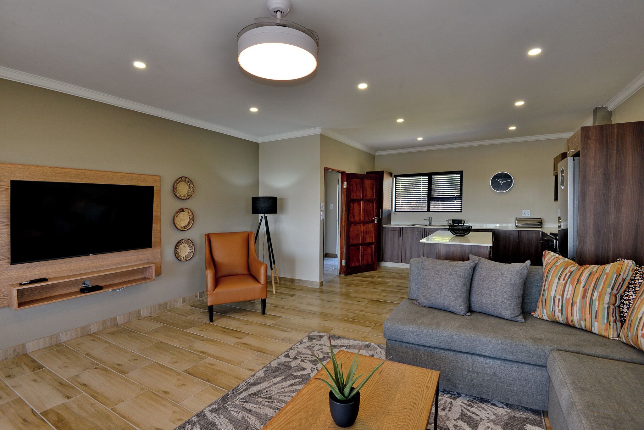 A modern living room with a flat-screen TV, a sofa, a coffee table, and a potted plant.