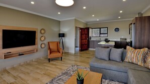 A modern living room with a flat-screen TV, a sofa, a coffee table, and a potted plant. - Seasons Golf, Leisure & Spa (Hartbeespoort/ Brits)
