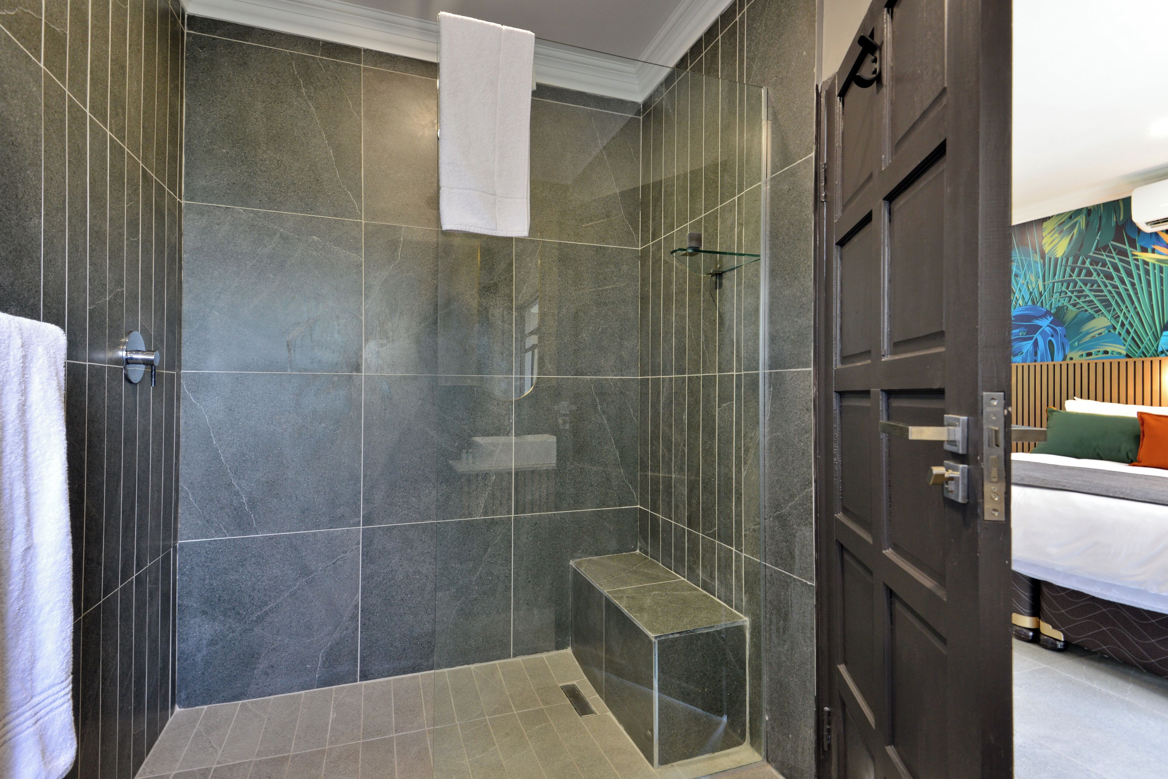Een moderne badkamer met een douche met glazen wand, een bankje en een handdoek aan de muur.