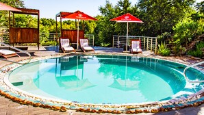 A swimming pool with lounge chairs and umbrellas, surrounded by a wooden deck and greenery. - Seasons Golf, Leisure & Spa (Hartbeespoort/ Brits)