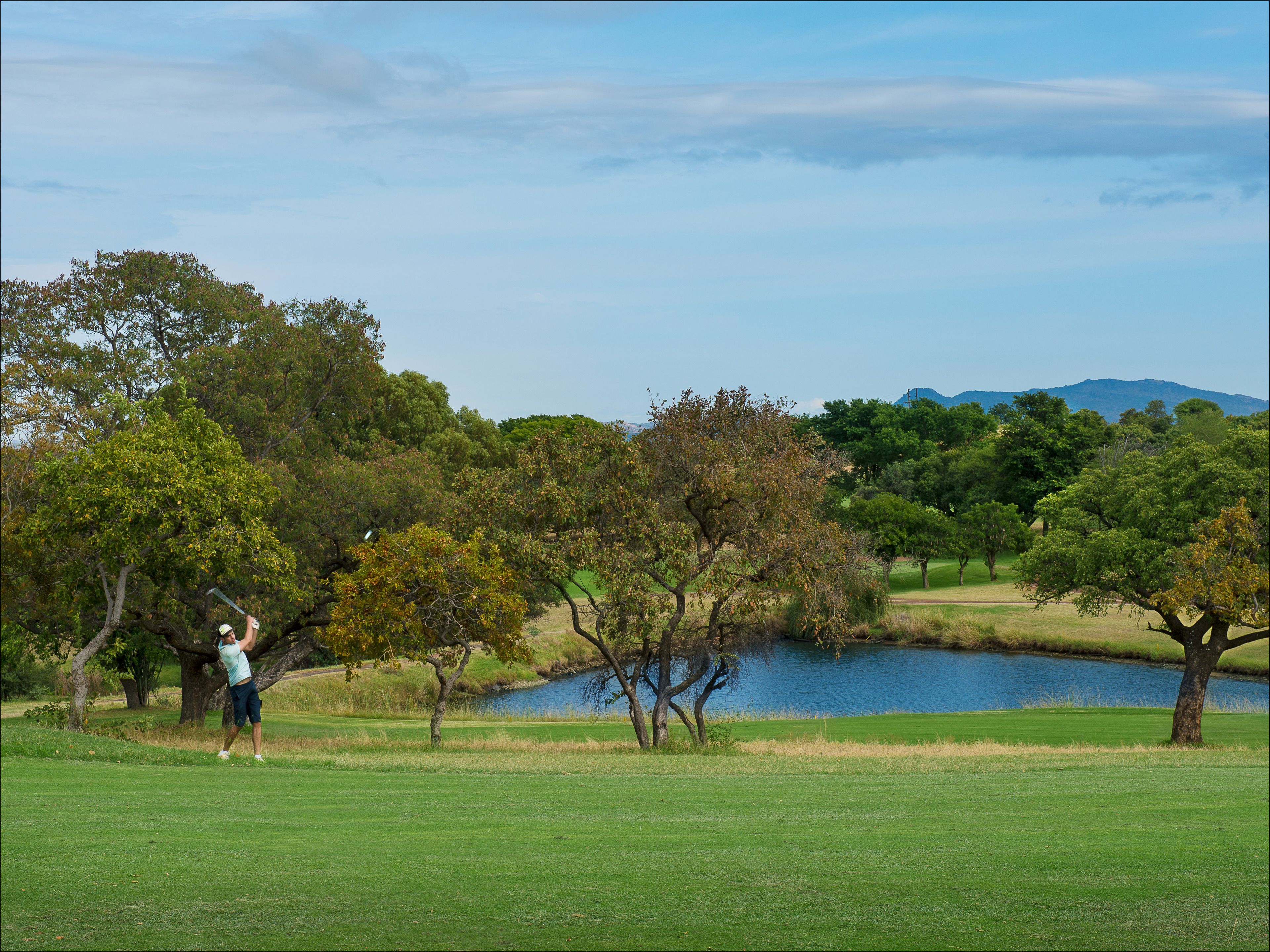 A golf course with a pond, trees, and a mountain in the background.