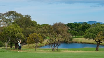 A golf course with a pond, trees, and a mountain in the background.