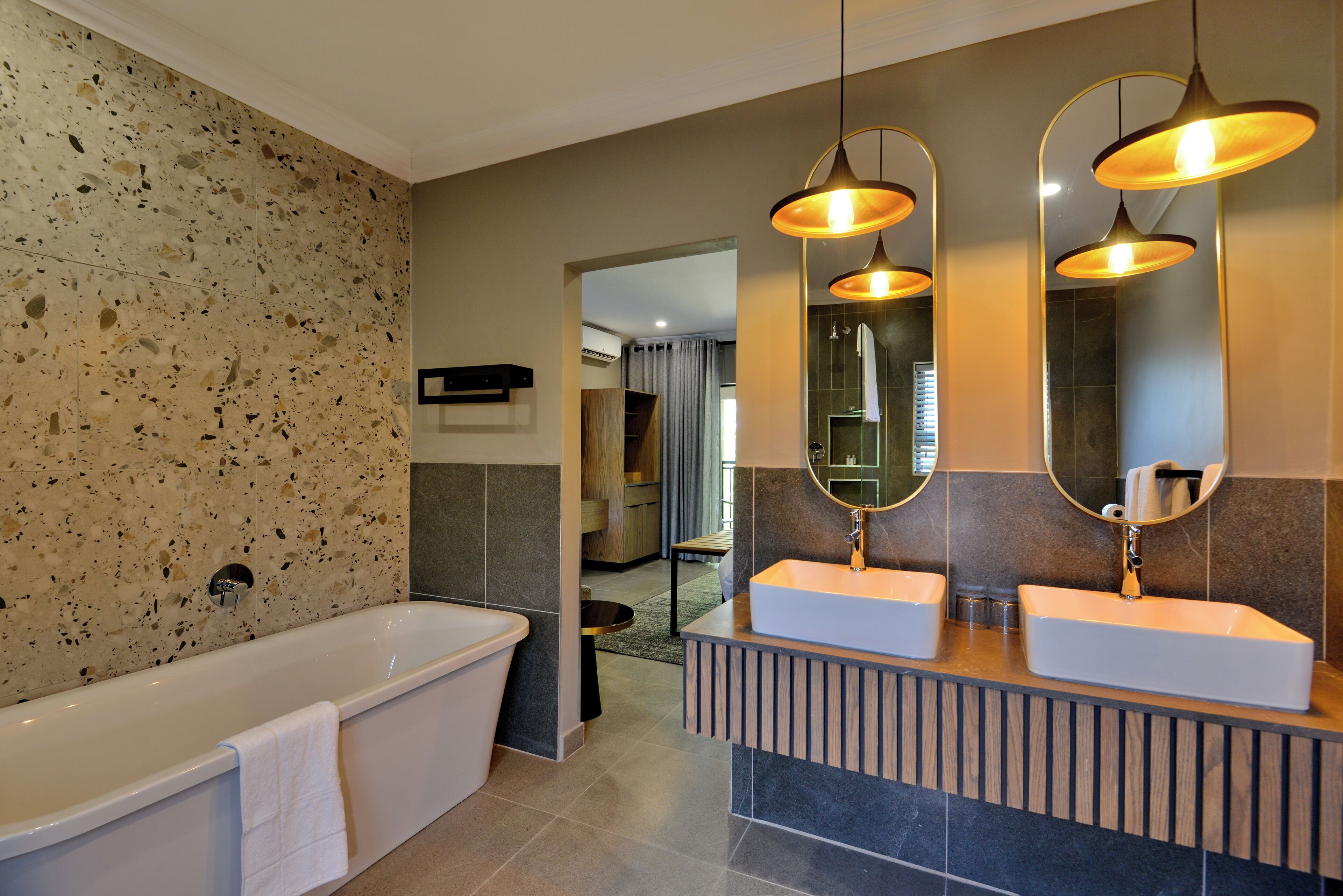 Un baño moderno con una bañera independiente, dos lavamanos con espejos e iluminación colgante.