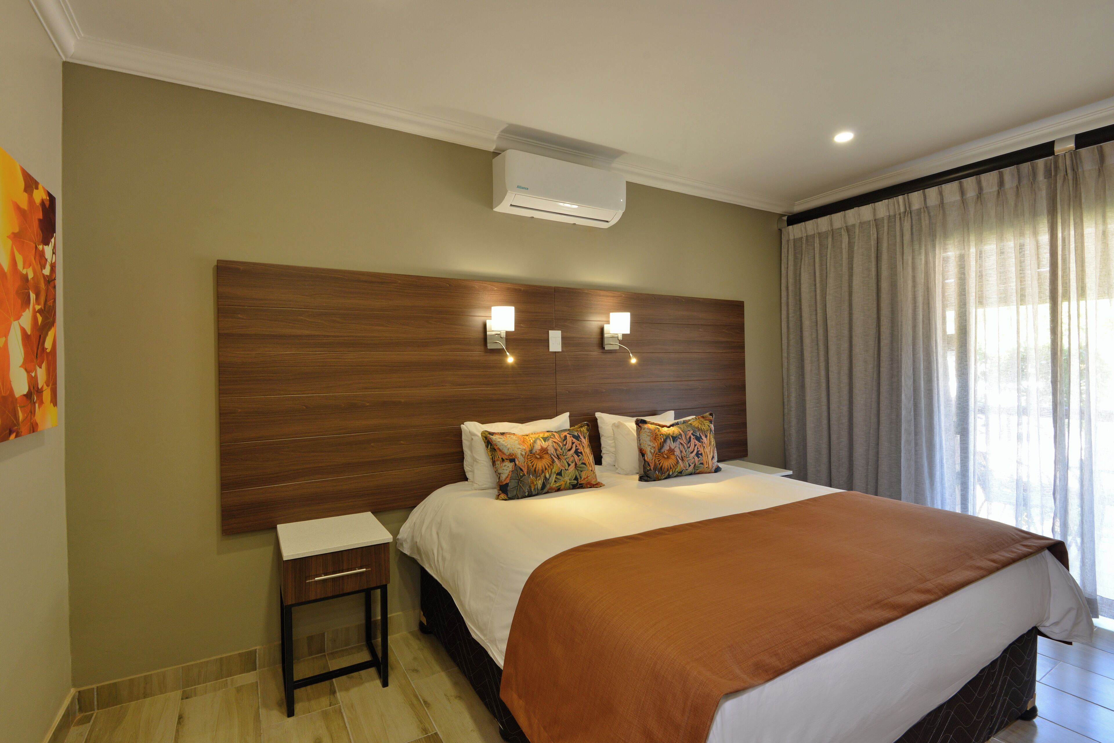 Quarto de hotel com cama grande, mesa de cabeceira, ar condicionado e janela com cortinas.