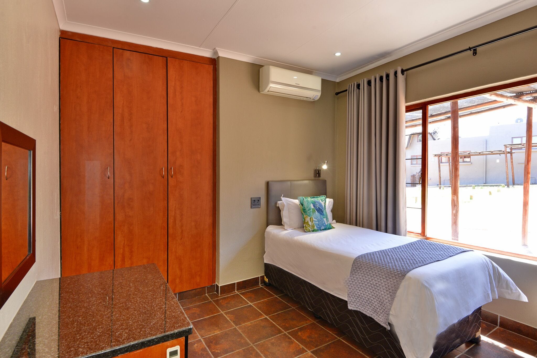 Habitación de hotel con una cama, un armario de madera, un equipo de aire acondicionado y una ventana con cortinas.