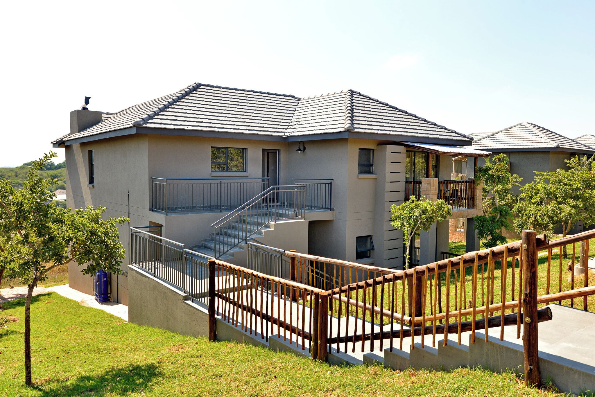 A modern two-story house with a grey exterior, a balcony, and a wooden staircase leading to the upper floor.