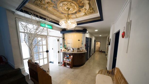 A hotel lobby with a reception desk, a chandelier, a staircase, and a bench. - Beewon Guest House - Hostel (Seoul)