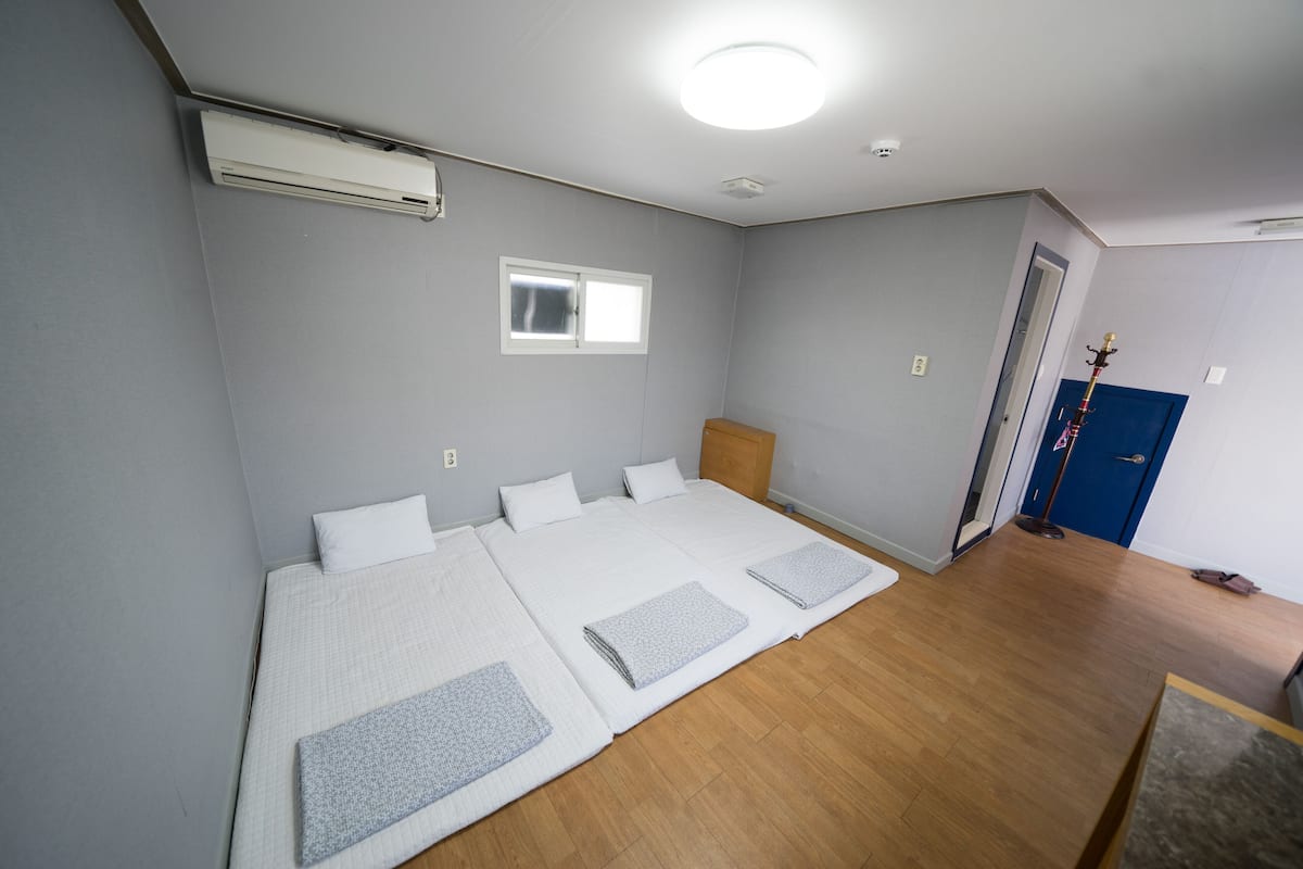 A room with two beds, a window, an air conditioner, and a wooden floor.
