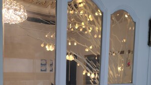 A room with a white door featuring multiple glass panels. Inside, there is a wicker chair and a table with a lamp. - Beewon Guest House - Hostel (Seoul)