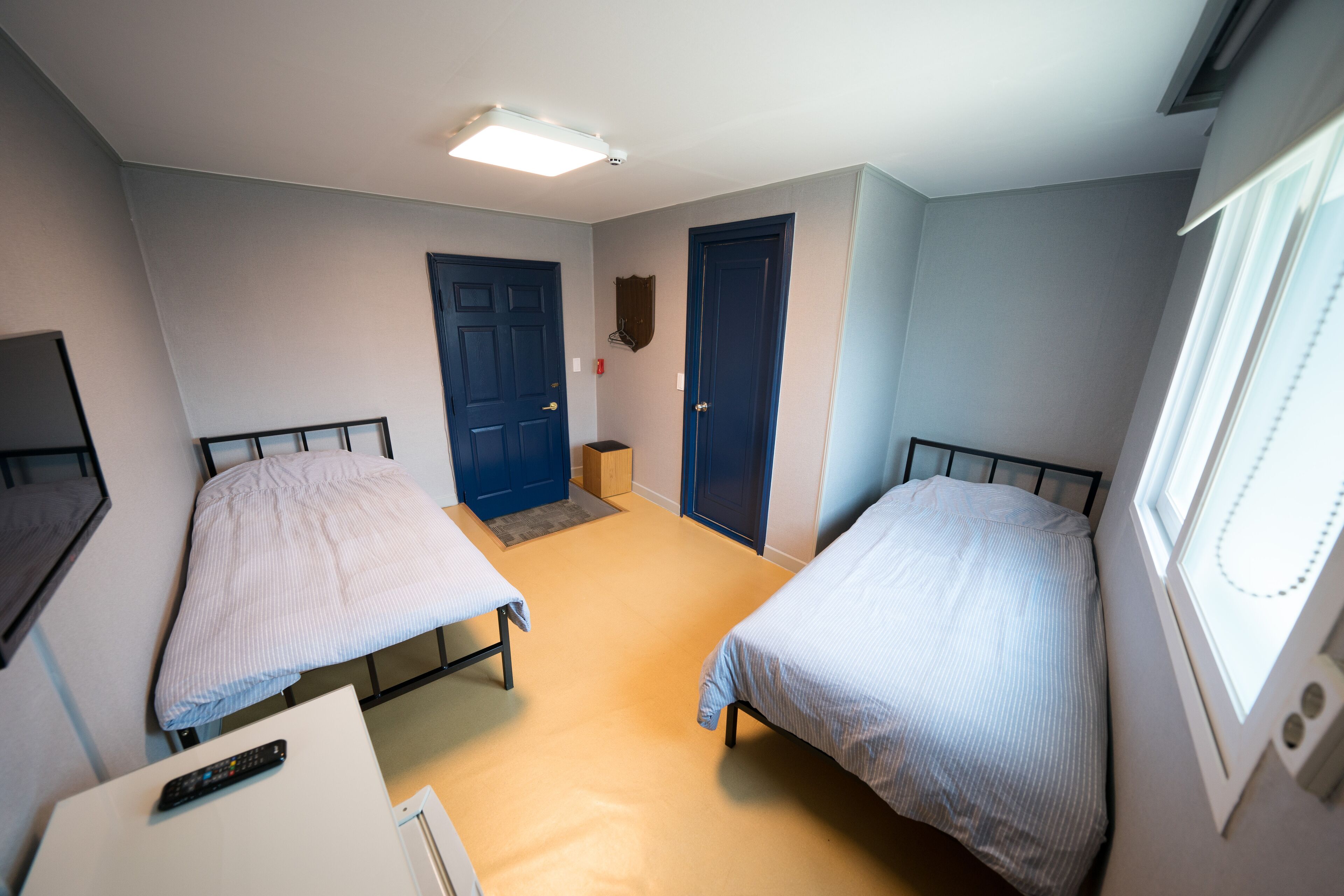 Ein Zimmer mit zwei Betten, einem Schreibtisch, einem Fernseher und einer Tür.