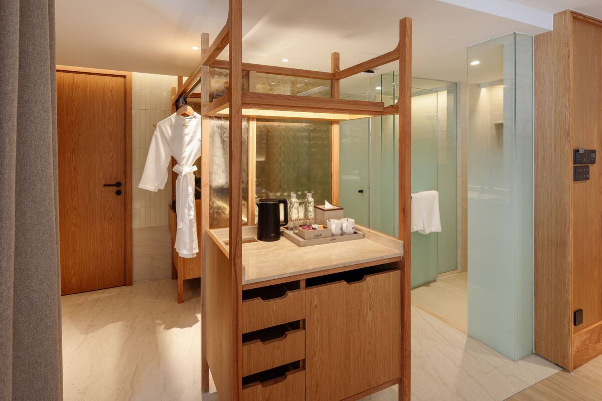 A modern bathroom with a wooden vanity, a glass shower enclosure, and a robe hanging on a rack.