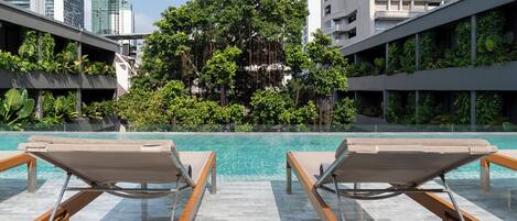 A rooftop pool with lounge chairs, surrounded by greenery and modern buildings.