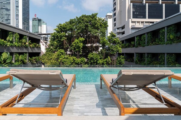 A rooftop pool with lounge chairs, surrounded by greenery and modern buildings. - Ad Lib Hotel Bangkok (Bangkok)