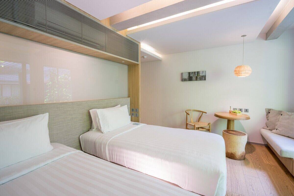 A modern hotel room with two beds, a sofa, a small table, and a hanging light fixture.