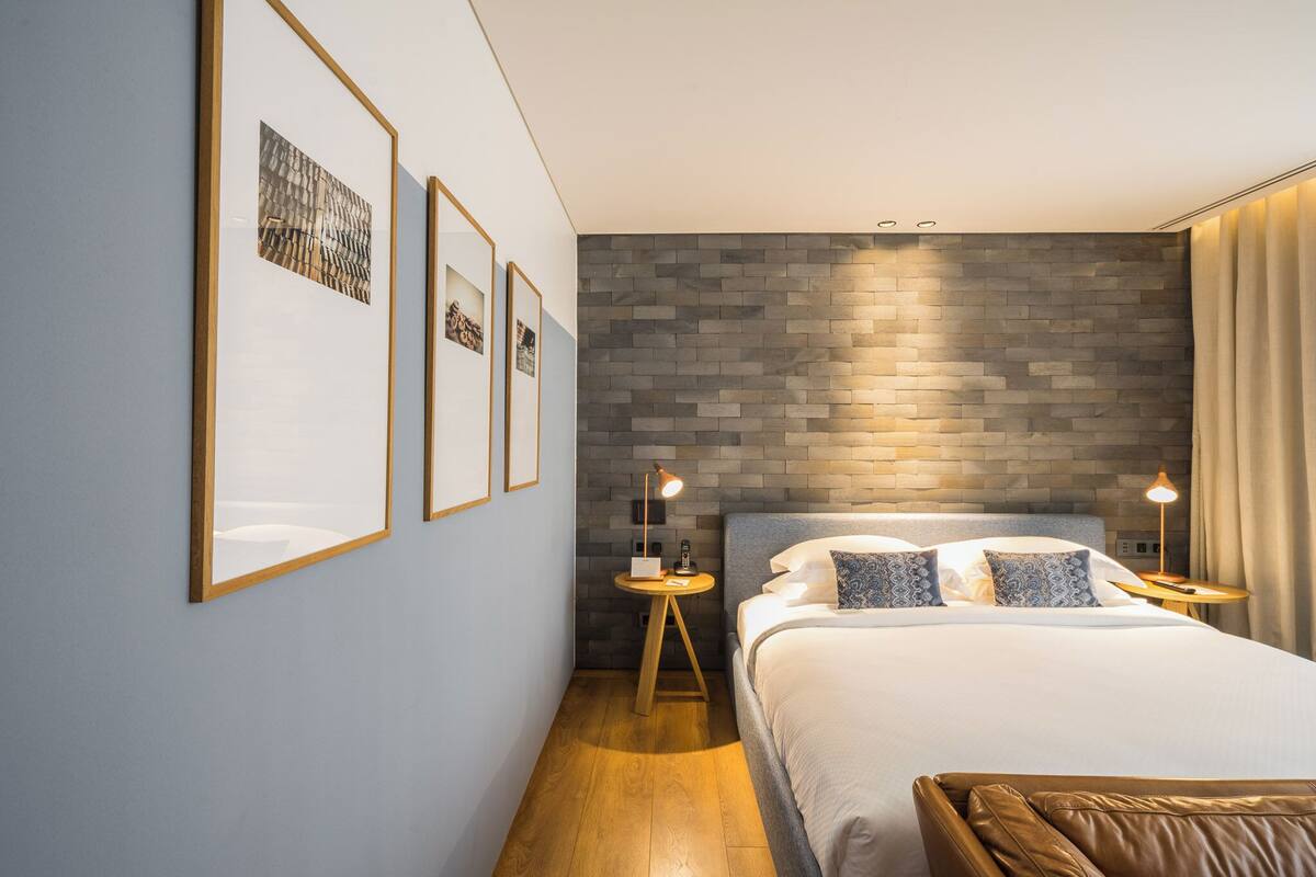 A modern hotel room with a large bed, two bedside tables, and a brick-patterned accent wall.