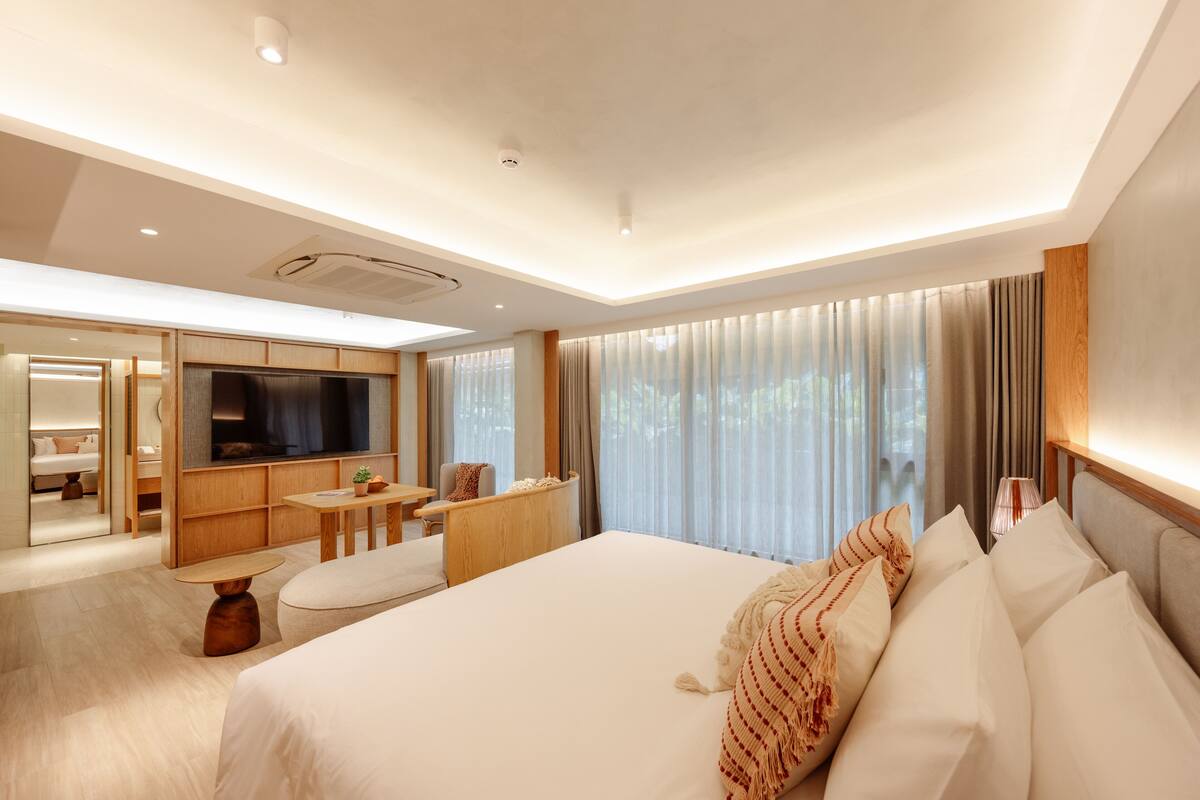 A modern hotel room with a large bed, a TV, a desk, and a seating area.
