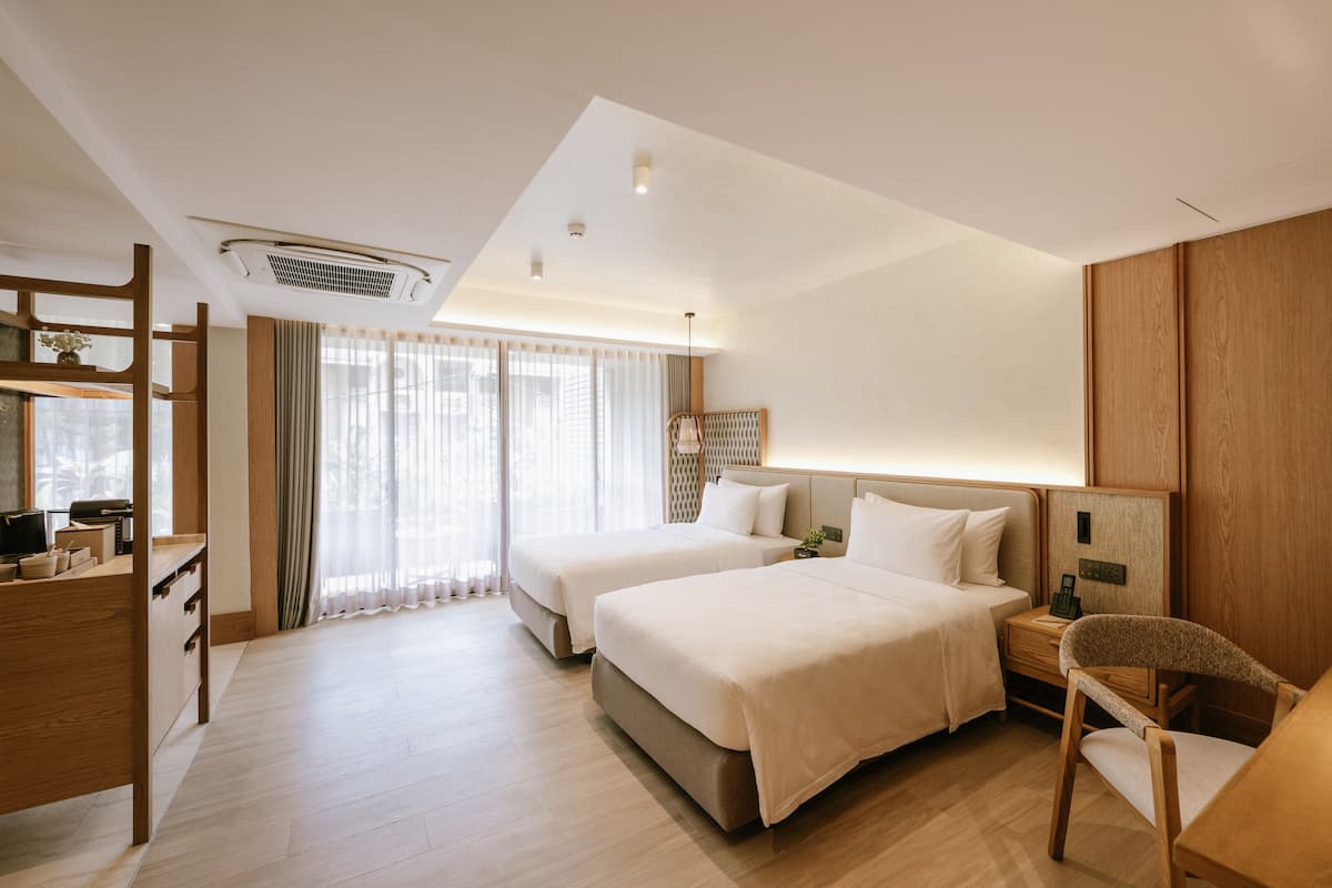 A hotel room with two beds, a desk, a chair, and a large window with curtains.