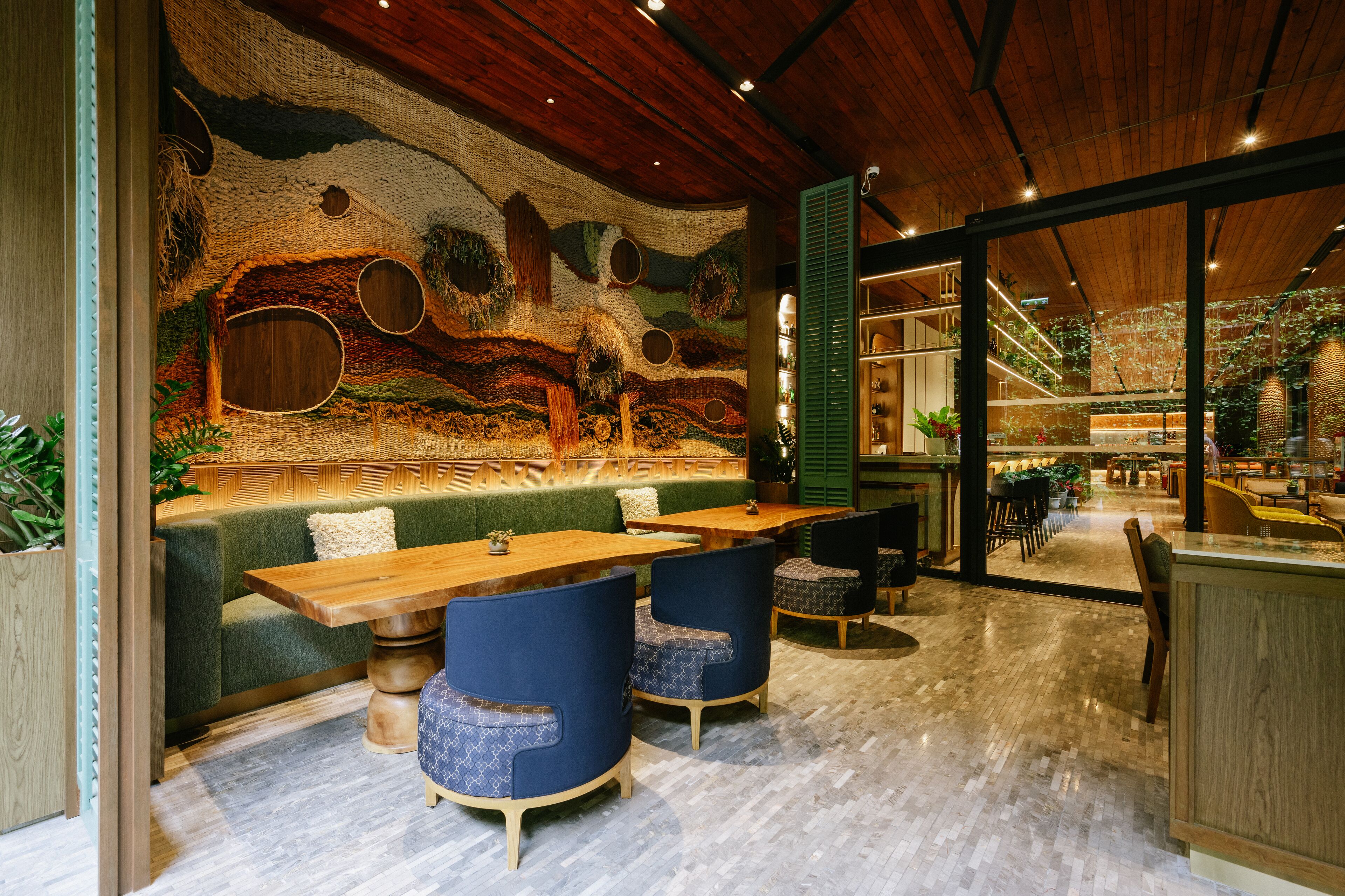 A restaurant with a rustic wooden ceiling, a green cushioned bench, and blue upholstered chairs.