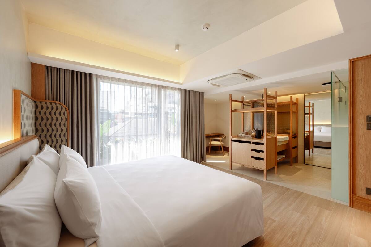 A hotel room with a large bed, a desk, a wardrobe, and a bathroom visible through a glass partition.