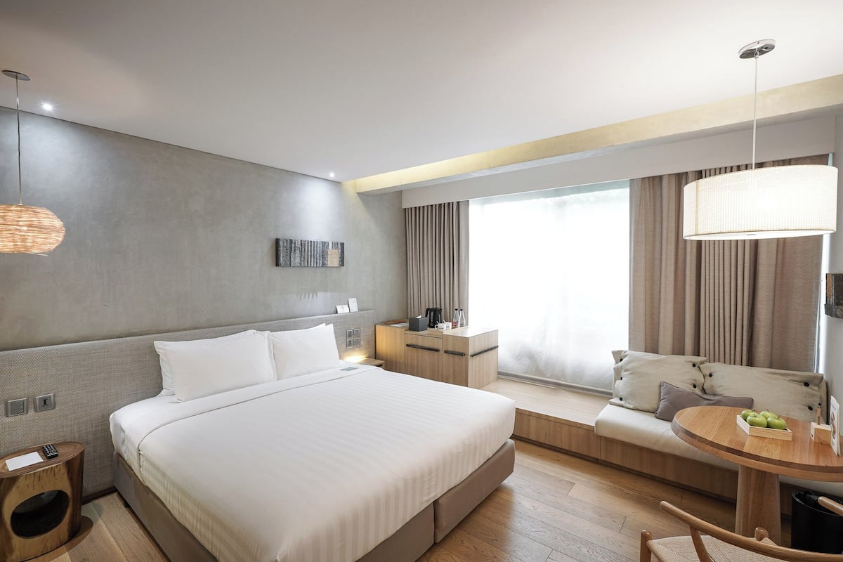 A modern hotel room with a large bed, a small desk, a round table, and a sofa.