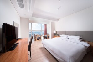 A modern hotel room with a large bed, a desk with a computer, a TV, a chair, and a small table. - Hotel Bareve (Seogwipo)