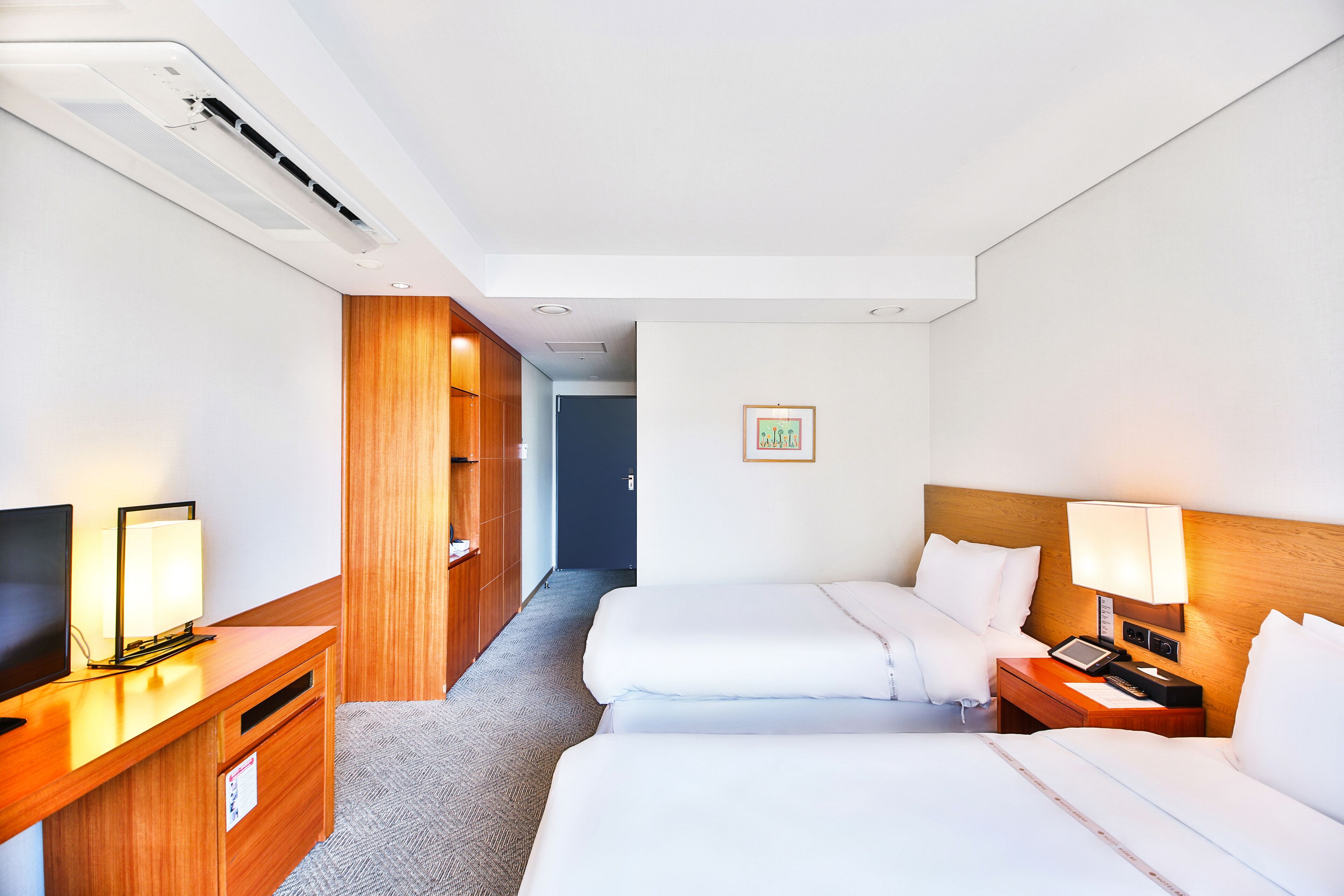 Een hotelkamer met twee bedden, een bureau met een televisie, een lamp en een houten garderobe.