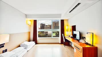 A hotel room with a bed, desk, computer, and a window with a view of buildings.