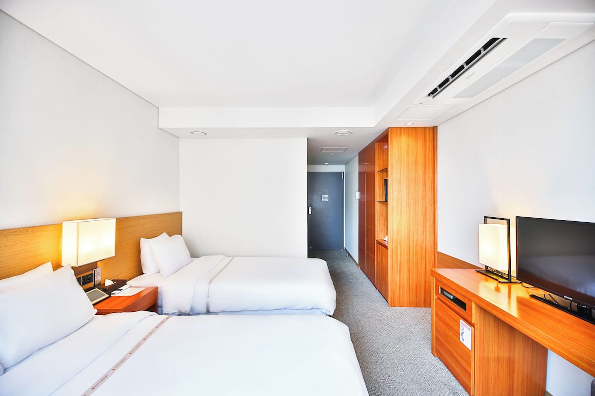 A hotel room with two beds, a TV, a desk, and a wardrobe.