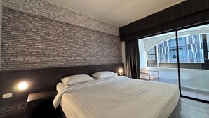 Una habitació d'hotel moderna amb paret de relleu de maó, un llit gran amb roba de llit blanca, una nit de nit amb una làmpada i vista a un paisatge urbà a través d'una finestra gran.