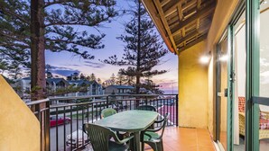 A balcony with a table and chairs, overlooking a street with parked cars and houses. - Cottesloe Beach Chalets (Cottesloe)