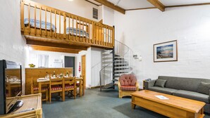 A cozy living room with a wooden dining table, chairs, a sofa, a staircase, and a framed picture on the wall. - Cottesloe Beach Chalets (Cottesloe)