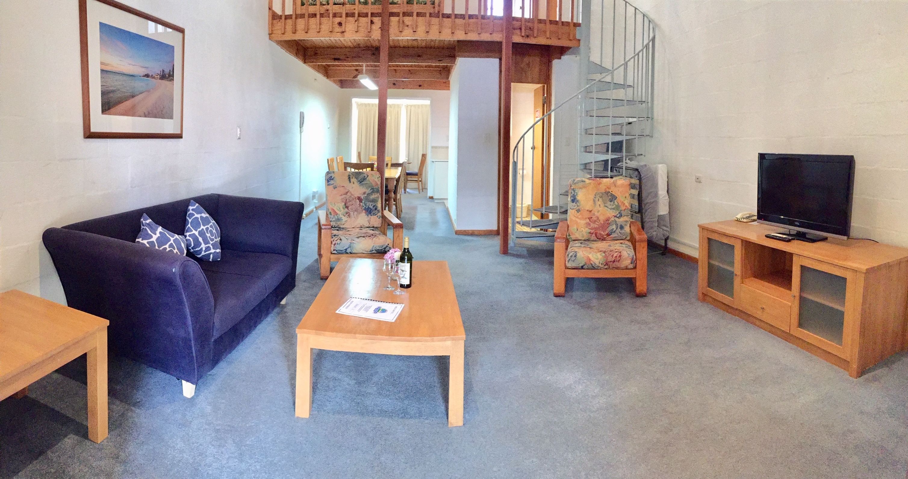 A living room with a sofa, two chairs, a coffee table, a TV, and a staircase.