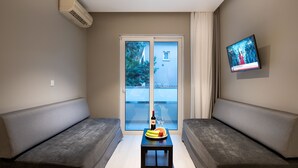 A modern living room with two grey sofas, a small table with a bottle and glasses, and a TV mounted on the wall. - Sunday Hotel (Rhodes)